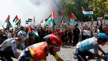 The pack rides as Pro-Palestinians protesters hold Palestinian flags during the 20th stage of the Vuelta a Espana 2025, a 156 km race between Robledo de Chavela and Bola del Mundo, in El Escorial, on September 13, 2025.   
Pierre-Philippe MARCOU / AFP