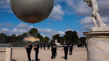 French police officers walk past the Paris 2024 Olympic and Paralympic Games cauldron attached to a balloon carrying the Olympic flame in the Tuileries garden in Paris, on August 7, 2024, during the Paris 2024 Olympic and Paralympic Games.  
JOEL SAGET / AFP