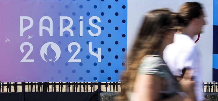 epa11483392 People walk past a sign with the Paris 2024 logo in Paris, France, 17 July 2024. From 18 to 26 July, the day of the Opening Ceremony of the Paris 2024 Olympic Games, security measures will be put in place in the French capital along the Seine river's banks and quays ahead of the main event. The Summer Olympics are scheduled to take place from 26 July to 11 August 2024 in Paris.  EPA/TERESA SUAREZ