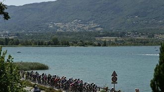 The pack of riders (peloton) cycles past Lac du Bourget lake at the start of the 17th stage of the 113th edition of the Tour de France cycling race, 174,7 km between Chambéry and Voiron in the French Alps, on July 22, 2026. 
Loic VENANCE / AFP