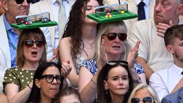 Two spectators sporting hats in the shape of a tennis court, clap during the men's singles final tennis match on the fourteenth day of the 2026 Wimbledon Championships at The All England Lawn Tennis and Croquet Club in Wimbledon, southwest London, on July 12, 2026. 
Kirill KUDRYAVTSEV / AFP